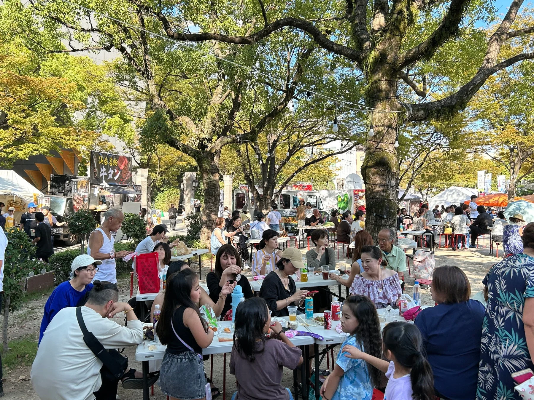 公園で開催されている屋外イベントで、多くの人々が食事を楽しむ様子